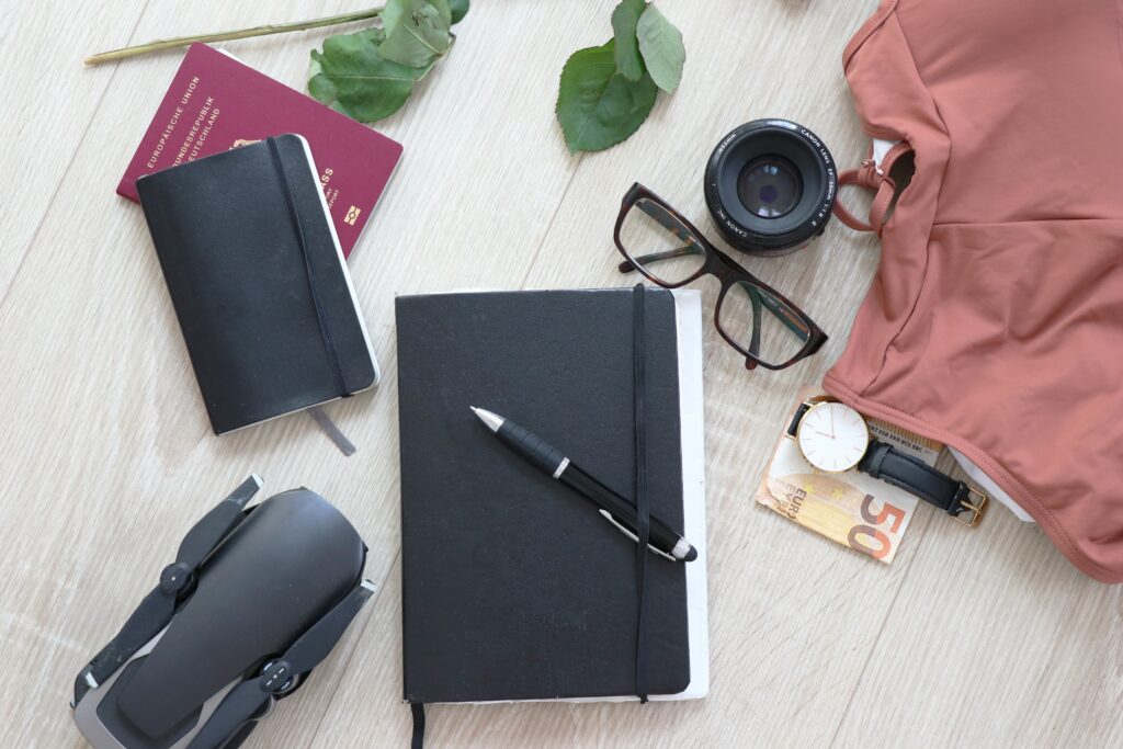 A flatlay showing how a photographer would pack minimally, with one notebook, basic equipment, a bathing suit and glasses. 