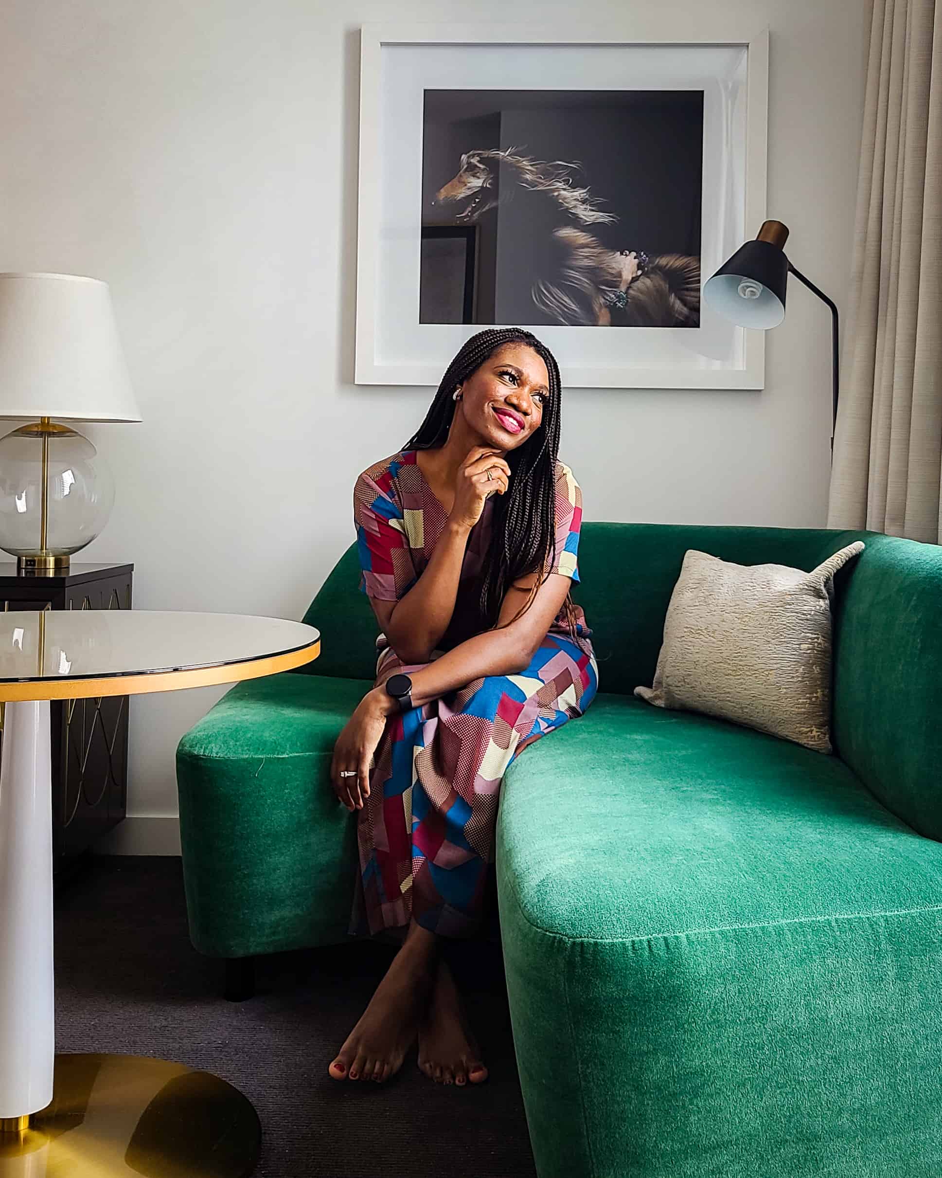 Chioma Ikoku sitting on a velvet green couch, gazing out of an unpictured window.