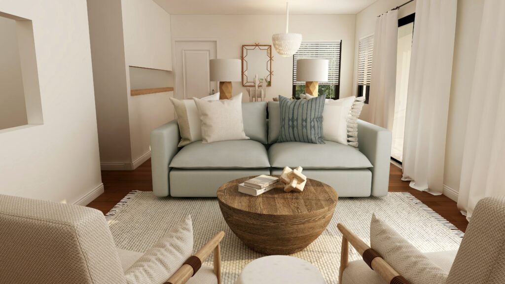 A small living room, with coastal inspired furniture. The view is of a pale green loveseat facing two linen armchairs. A polished wood drum table sits in the middle of an ivory braided rug. 