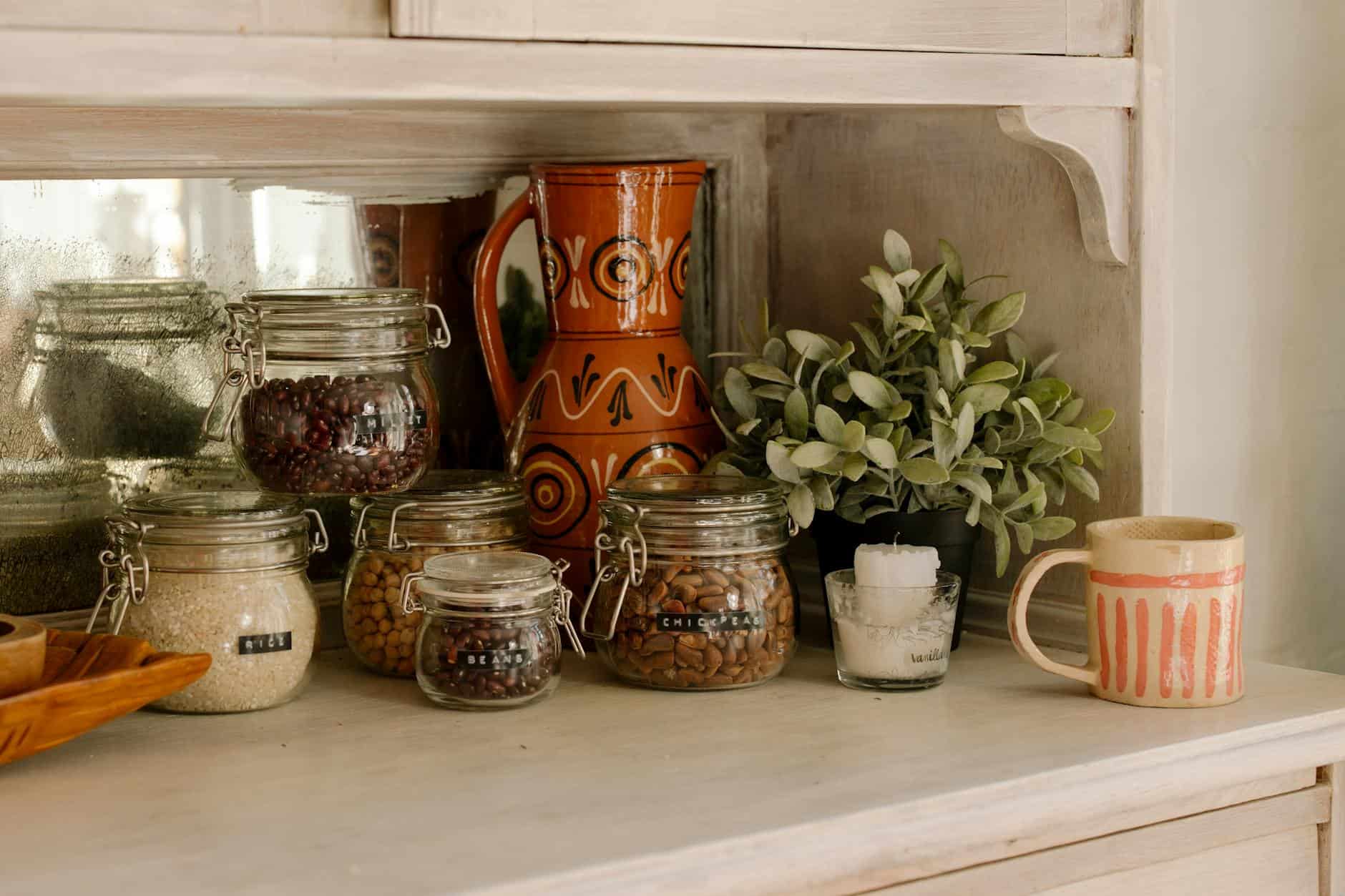 uniform glass food containers on a white shelf, styled with a hand-painted, brown ceramic vase with uneven glaze